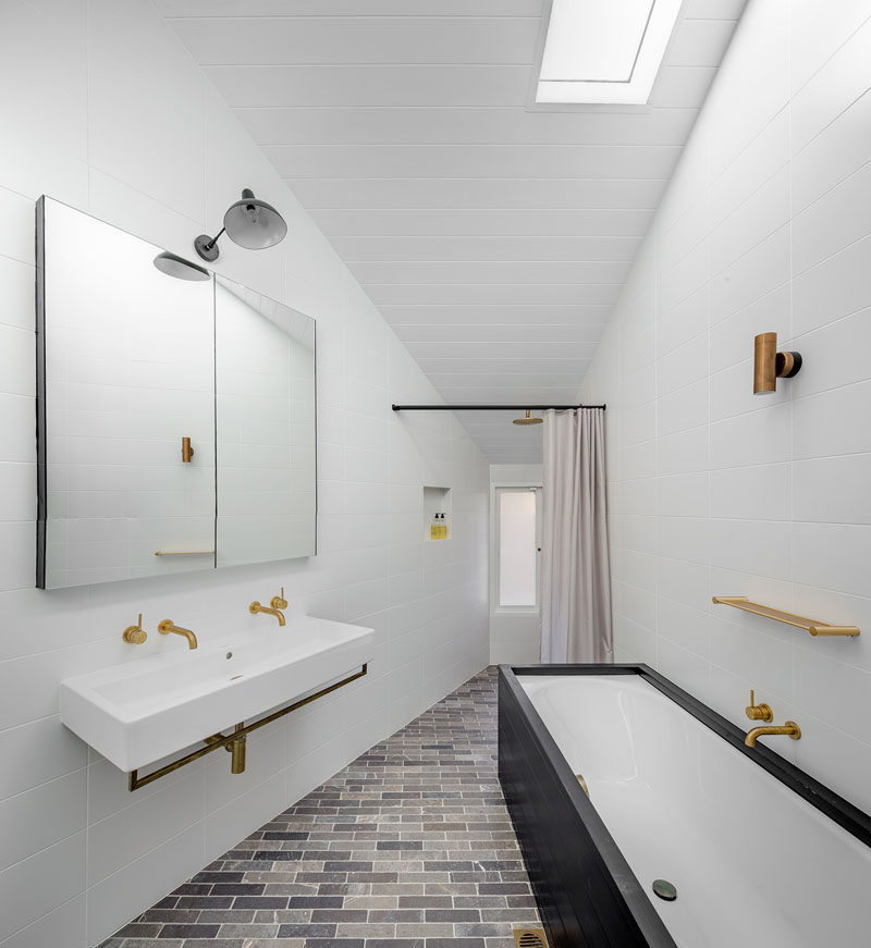 In this bathroom, white walls and ceilings make the brass accents and black cabinetry stand out. A skylight provides plenty of natural light to the space too.