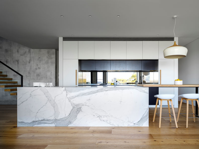 This kitchen pairs white cabinets with a large marble kitchen island, that connects to a wooden bar area with seating.