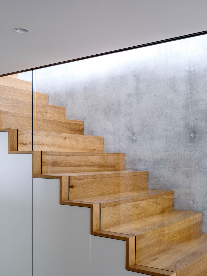 Wood stairs sandwiched between a concrete wall and glass safety railing guide you to the lower level of this home.