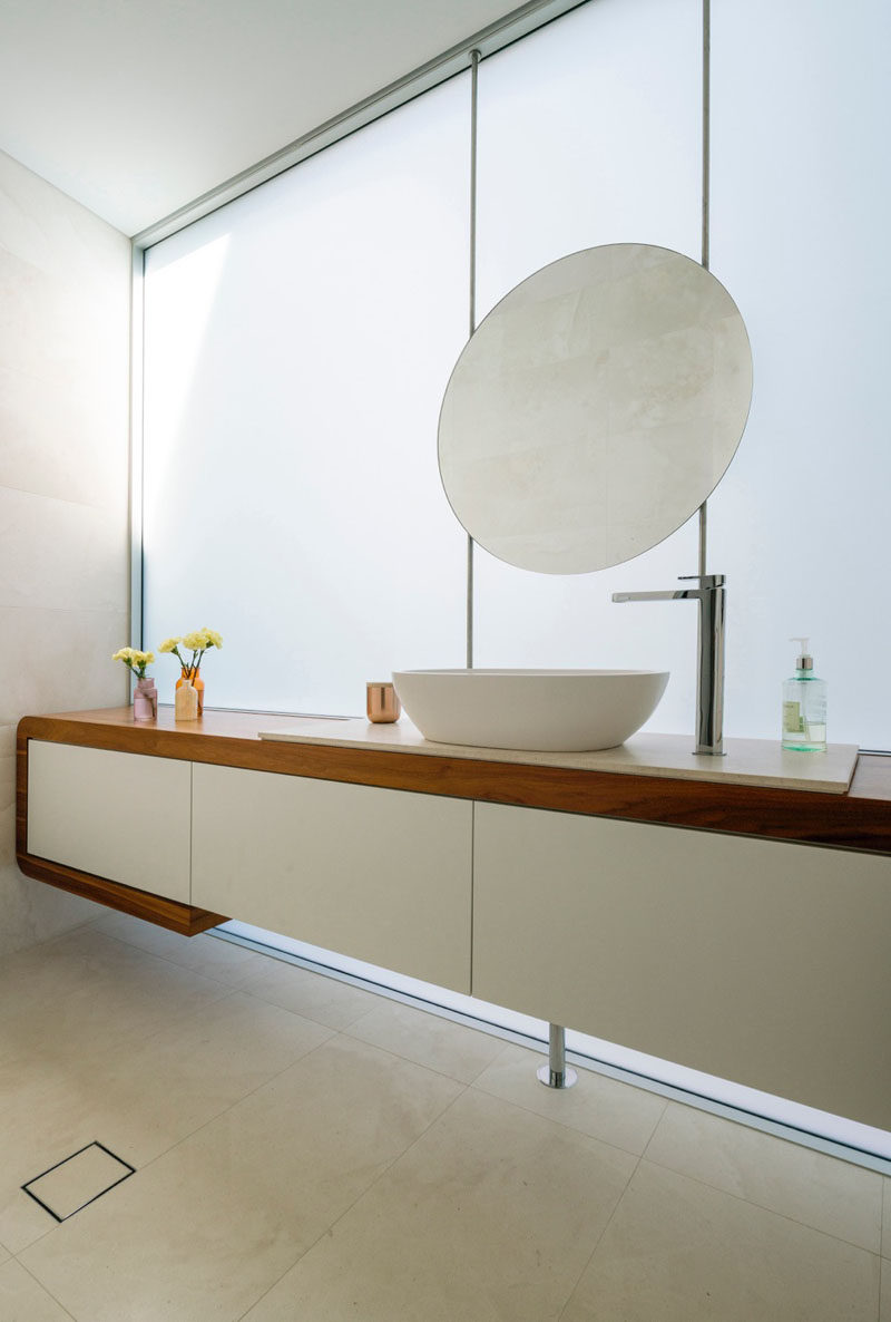 In this bathroom, a round mirror matches the curves on the oval sink, and the wood vanity breaks up the white found throughout the rest of the bathroom.