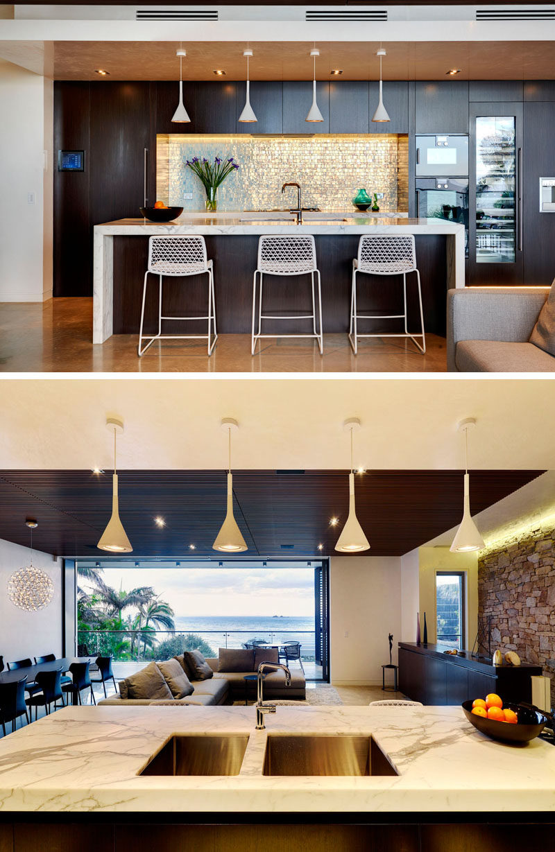 This kitchen has dark wood cabinetry, which contrasts the white kitchen island and overhead pendant lights.