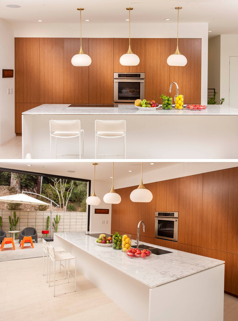 In this kitchen, three pendant lights anchor the mostly-white kitchen island, and wooden cabinetry adds a natural touch to the space.