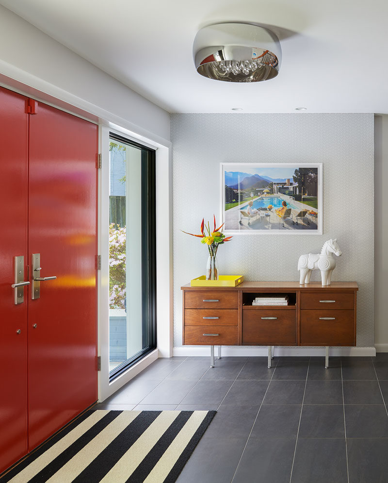 This home was renovated to include a bright red front door, with the foyer home to a mid-century modern style with a console table, a black and white striped rug and a framed retro photograph.