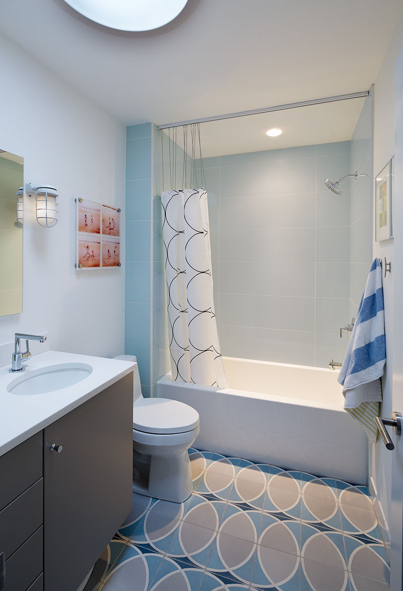 In this bathroom, light blue and gray create a serene look, with the circular pattern tile floor complementing the shower curtain and adds interest to the design.