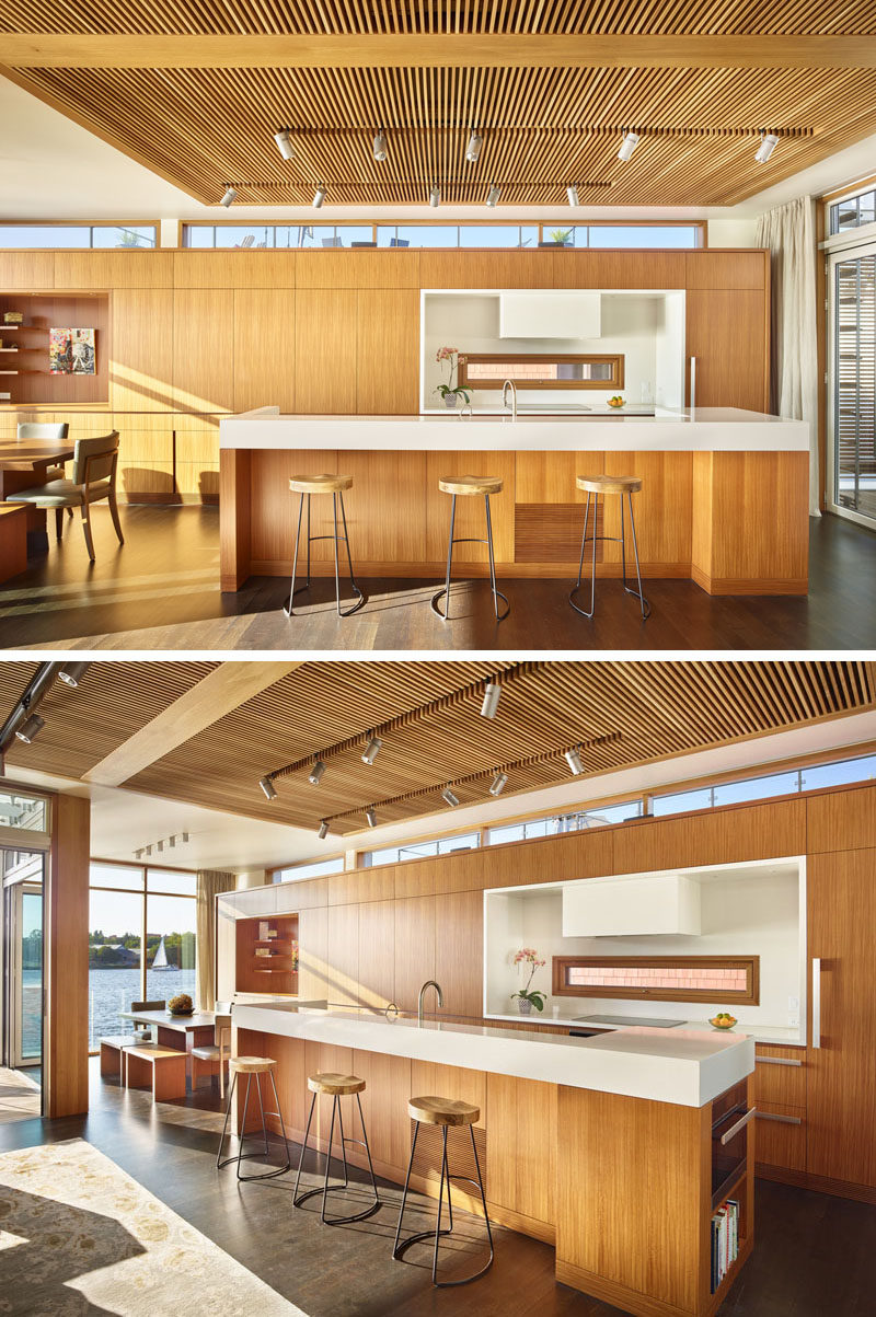 In this floating home, a wood slat ceiling feature anchors the living room and kitchen, and provides contrast to the surrounding white ceiling and walls. White touches has also been used in the kitchen, like on the island and cooktop area.