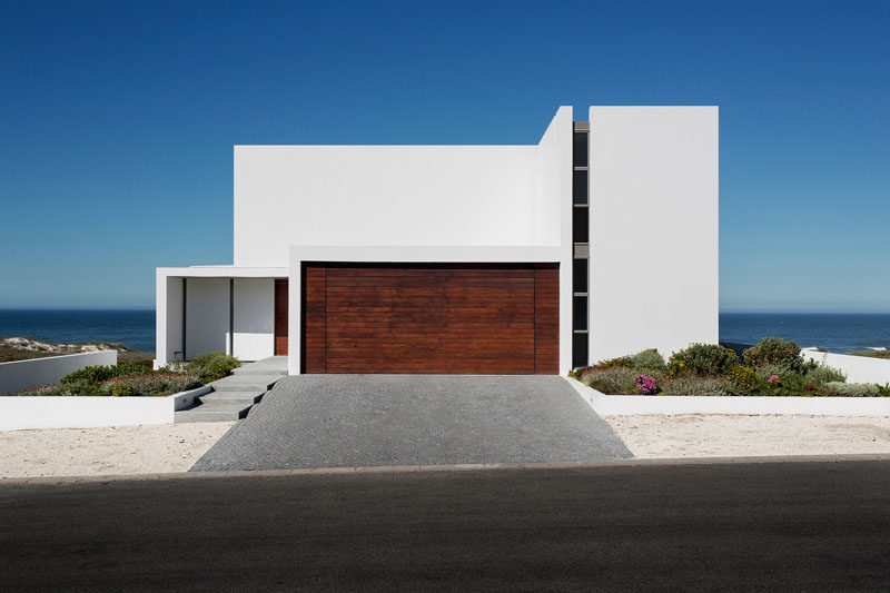 18 Inspirational Examples Of Modern Garage Doors // The dark wood paneled garage door is in stark contrast to the all white exterior and the light sand surrounding it.