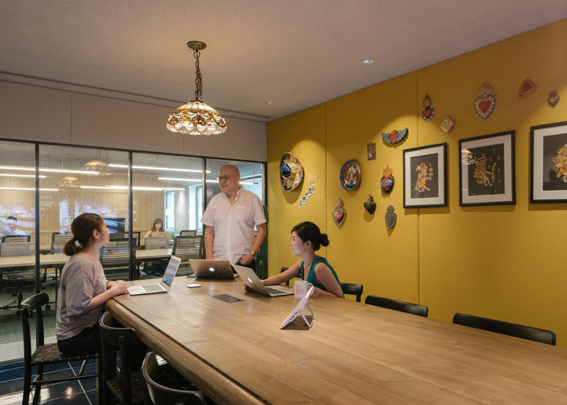 This boardroom has a bright yellow feature wall, large wooden table and a decorative pendant lamp.