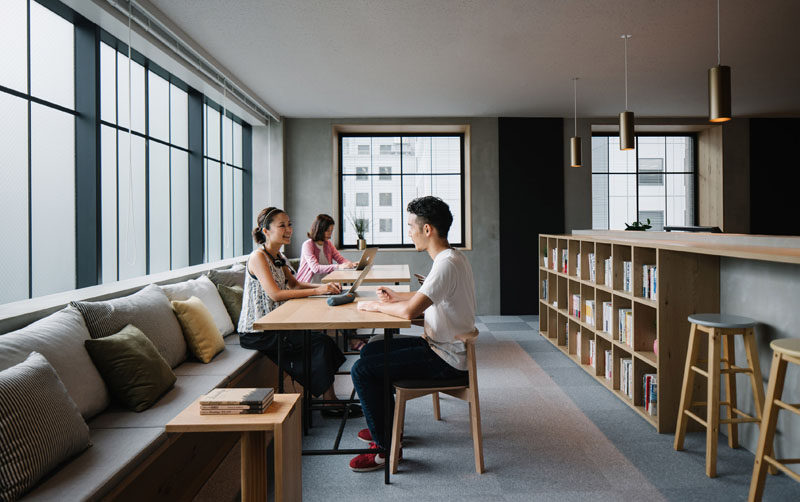 Running along the window in this office is a bench filled with cushions and communal work desks.