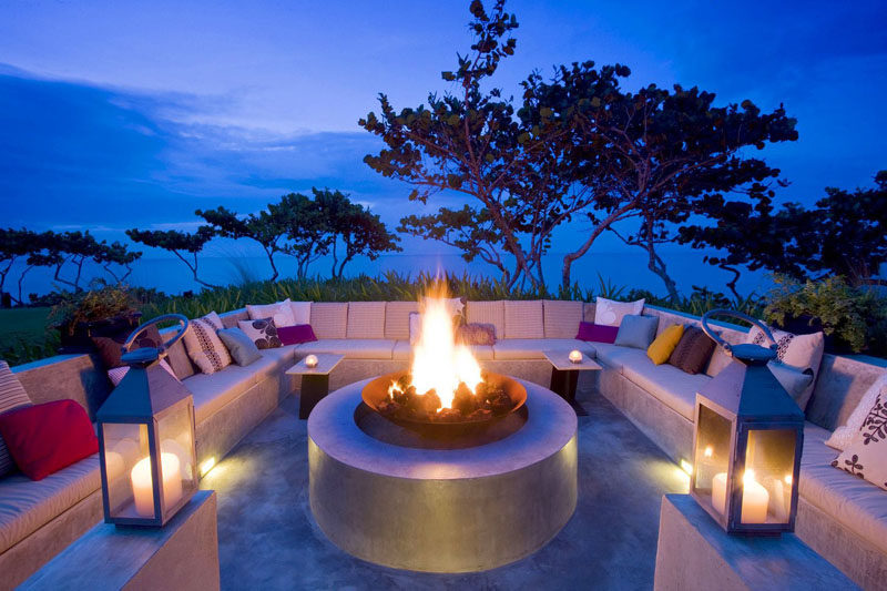 15 Outdoor Conversation Pits Built For Entertaining // Concrete benches covered in pillows surround a large fire pit that would throw off enough heat to let conversations flow late into the night. #ConversationPit #FirePit #YardIdeas