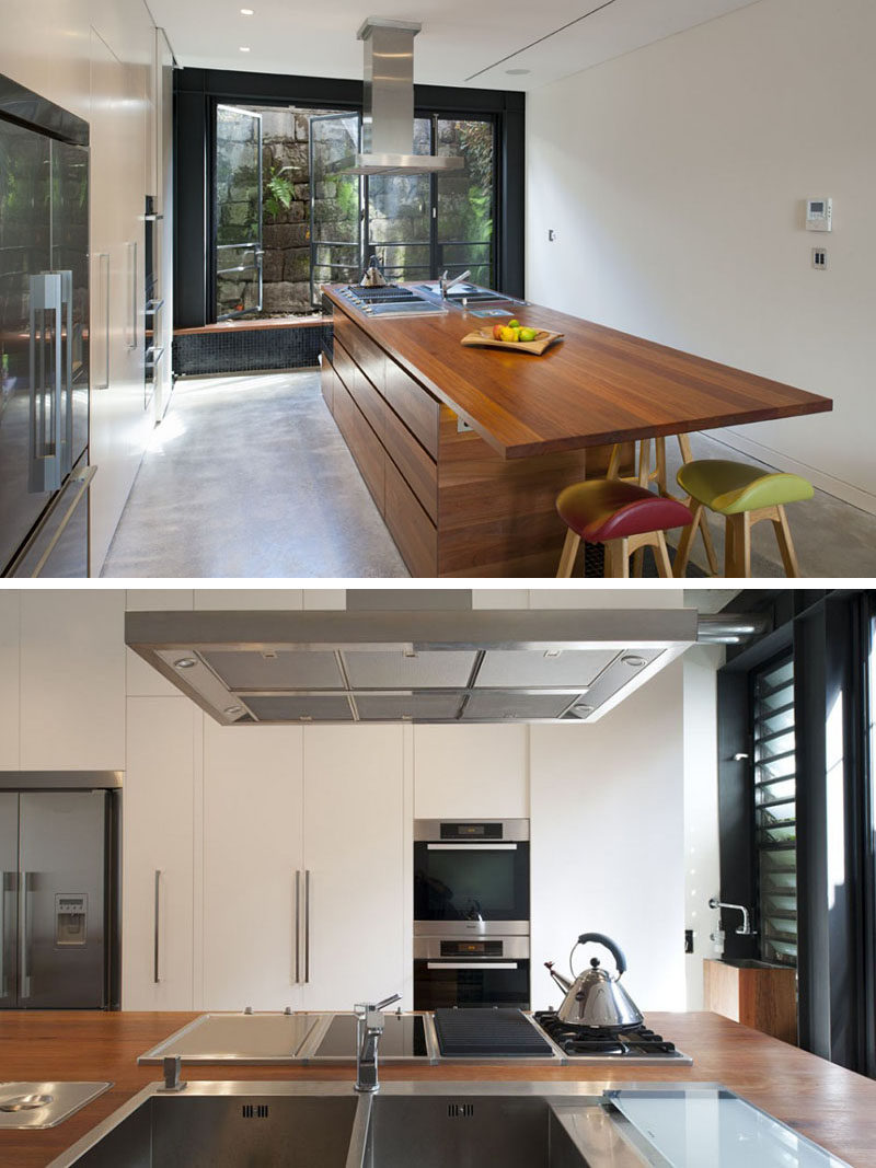 In this kitchen large windows open to assist with air flow, and a large wooden kitchen island is home to the cooktop, sink and bar area.