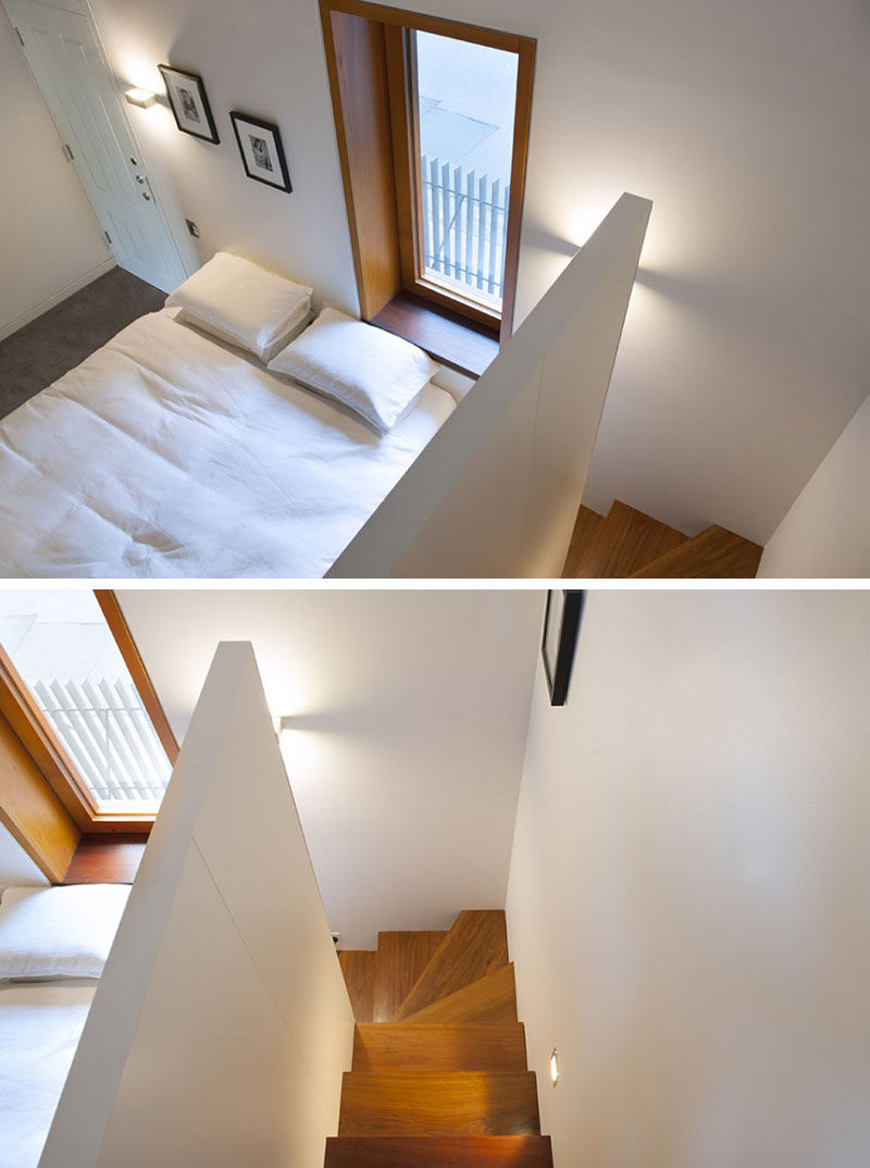 This bedroom has a wooden window frame and wooden stairs that contrast the white bedroom.