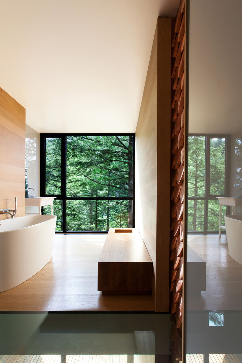 This bathroom has a large floor-to-ceiling window that provides views of the forest outside.