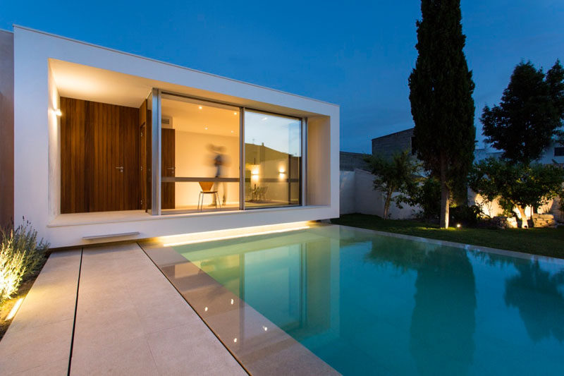 A small pool is positioned between a house and studio space, with lighting highlighting the dramatic design of the garden and patio.