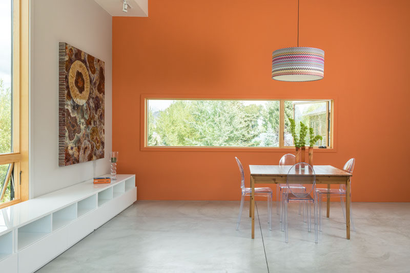 This dining area has a bright orange feature wall to draw your eye to the horizontal window.