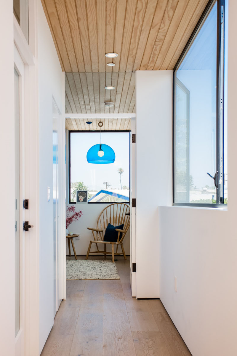 A bright blue pendant light guides to the bedroom in this all-white and wooden hallway.