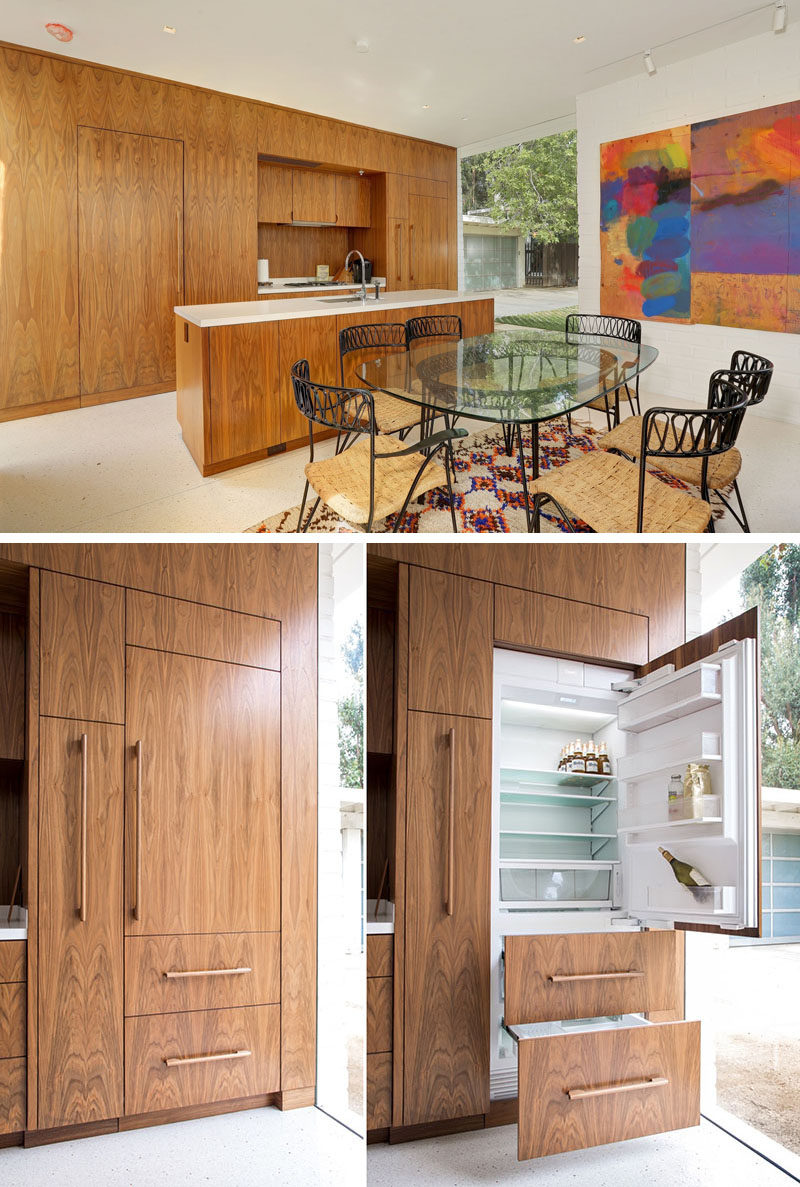 This kitchen has a long island with a lightly colored countertop that contrasts with the wood cabinetry. The hidden door on the left is a small powder room, and the door panel on the right is the integrated fridge.