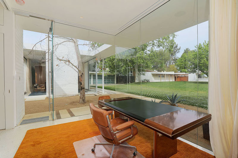 This home office with floor-to-ceiling glass windows looks out to the main house and the backyard.