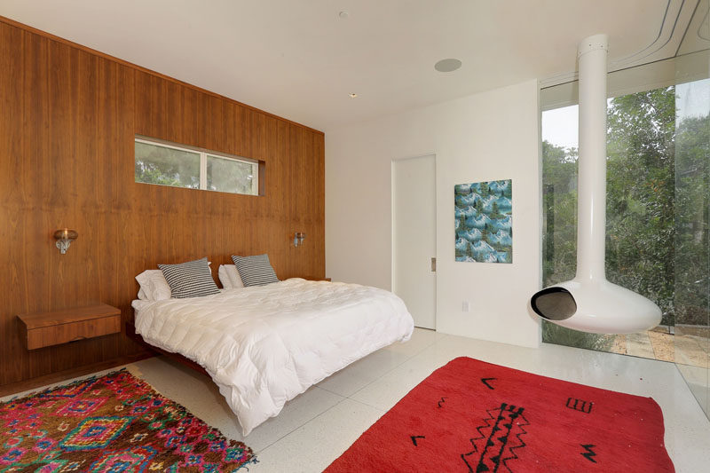 This bedroom has floor-to-ceiling windows, a wooden feature wall and a white hanging fireplace.