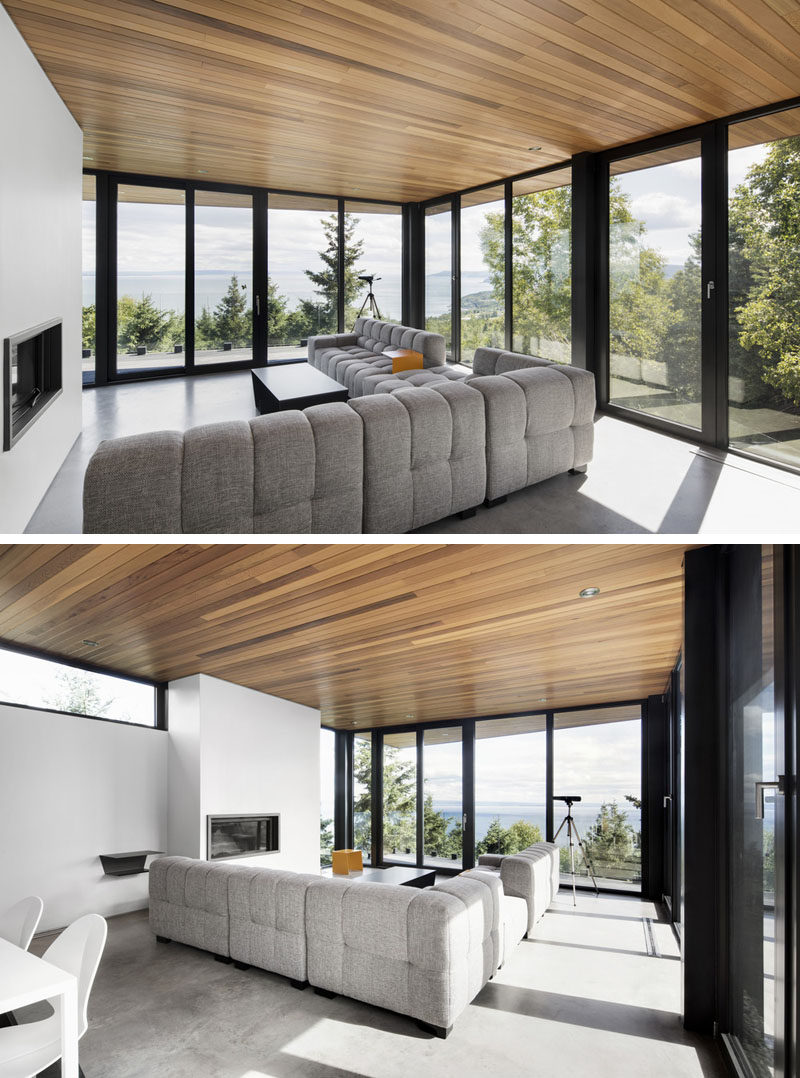 This living room is surrounded by black framed, floor-to-ceiling windows, with the large comfy couch focused on the fireplace.