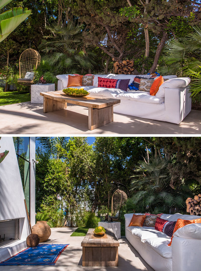 This outdoor space has been set up with a large white sofa and a wooden coffee table. Colorful accents have been added in the form of a blue rug and a few bright throw pillows.