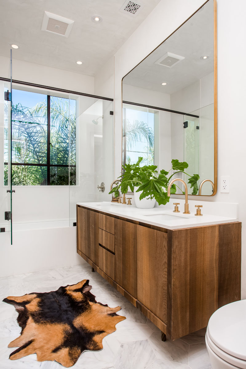 This bathroom combines wooden vanities, gold accents, white walls and plants, to create a contemporary look.