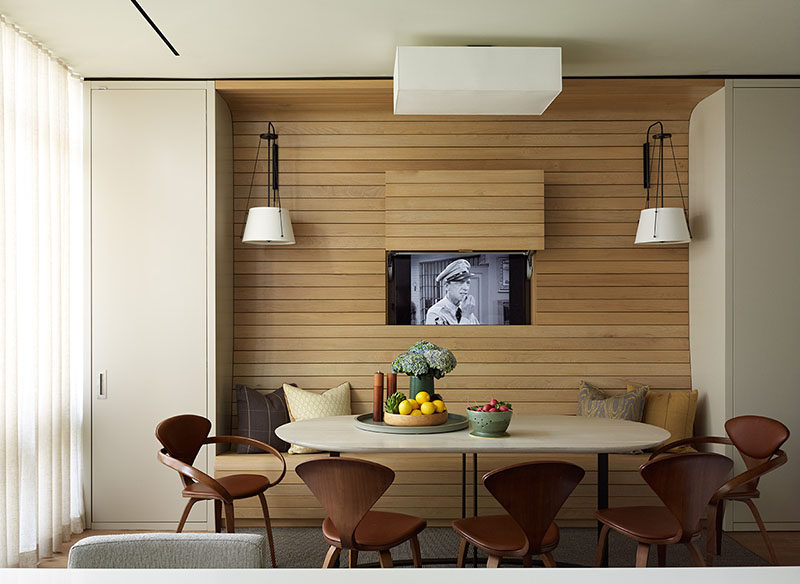 In this apartment, the television was placed behind a panel within the walnut wall, allowing it to be visible for when you want to watch tv, but at the same time, can be completely hidden away without the use of a bulky cabinet.