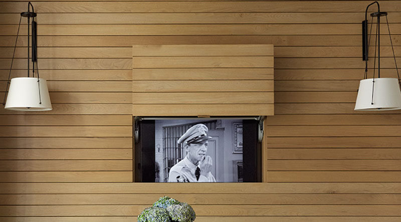 In this apartment, the television was placed behind a panel within the walnut wall, allowing it to be visible for when you want to watch tv, but at the same time, can be completely hidden away without the use of a bulky cabinet.