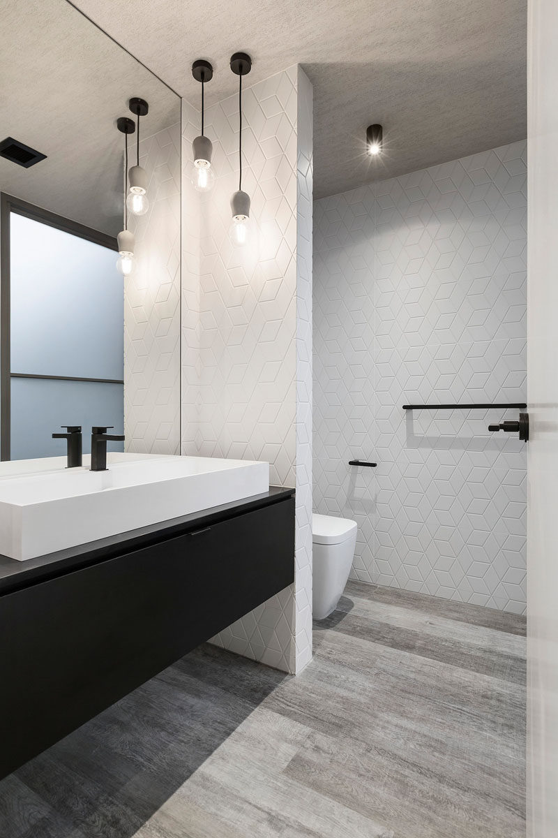 This mostly white bathroom with a black vanity, has simple pendant lights hanging in the corner.
