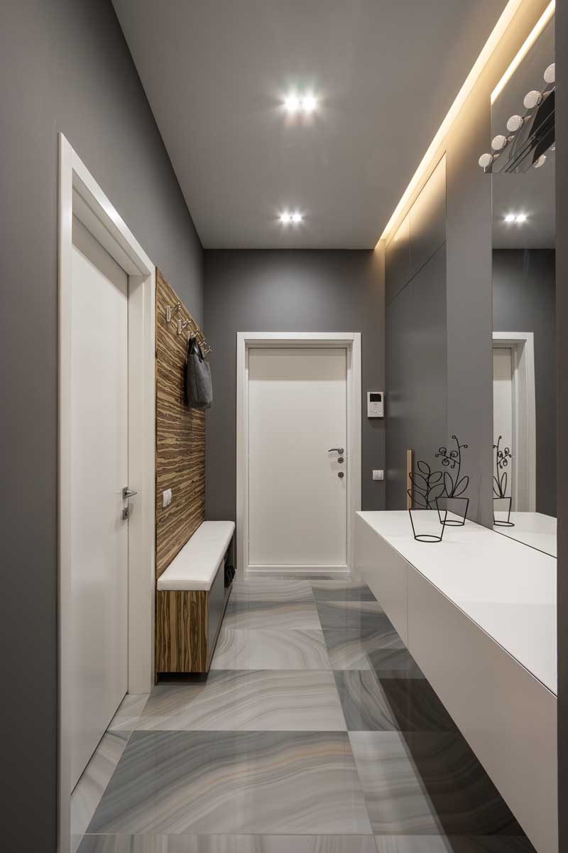 This grey entryway in this apartment has a slim built-in bench and wooden panel with hangers on one side, and on the opposite wall hangs a floating cabinet.