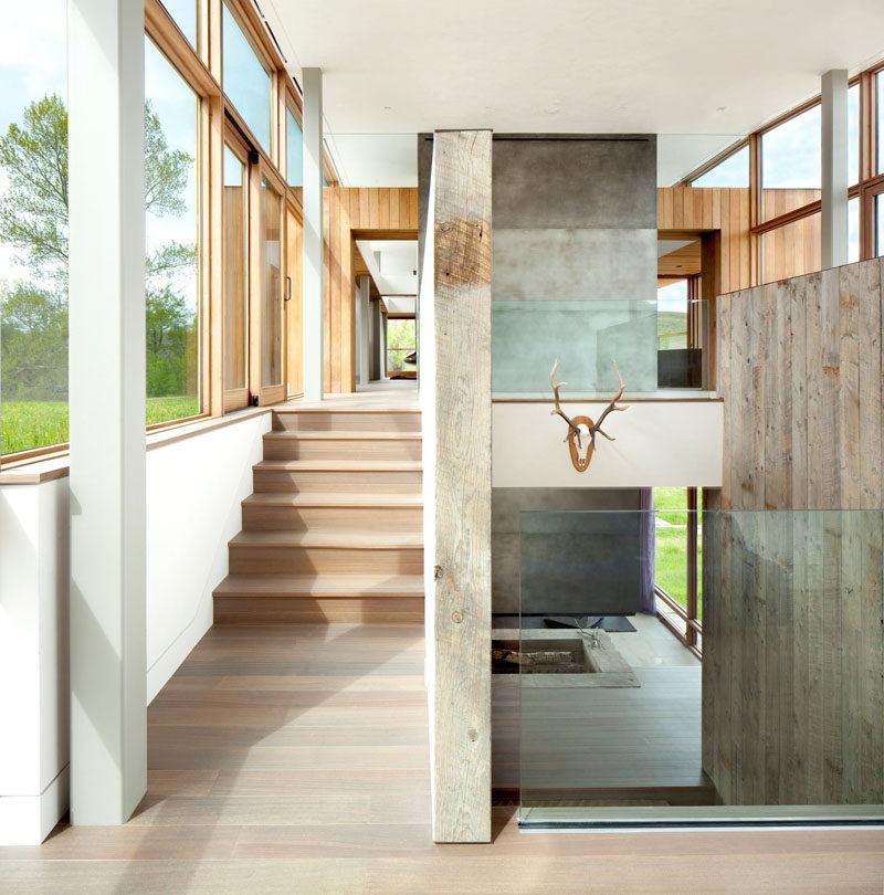 Large windows provide ample sunlight to these wooden stairs that have been paired with glass railings to guide you to the upper floor of the home.