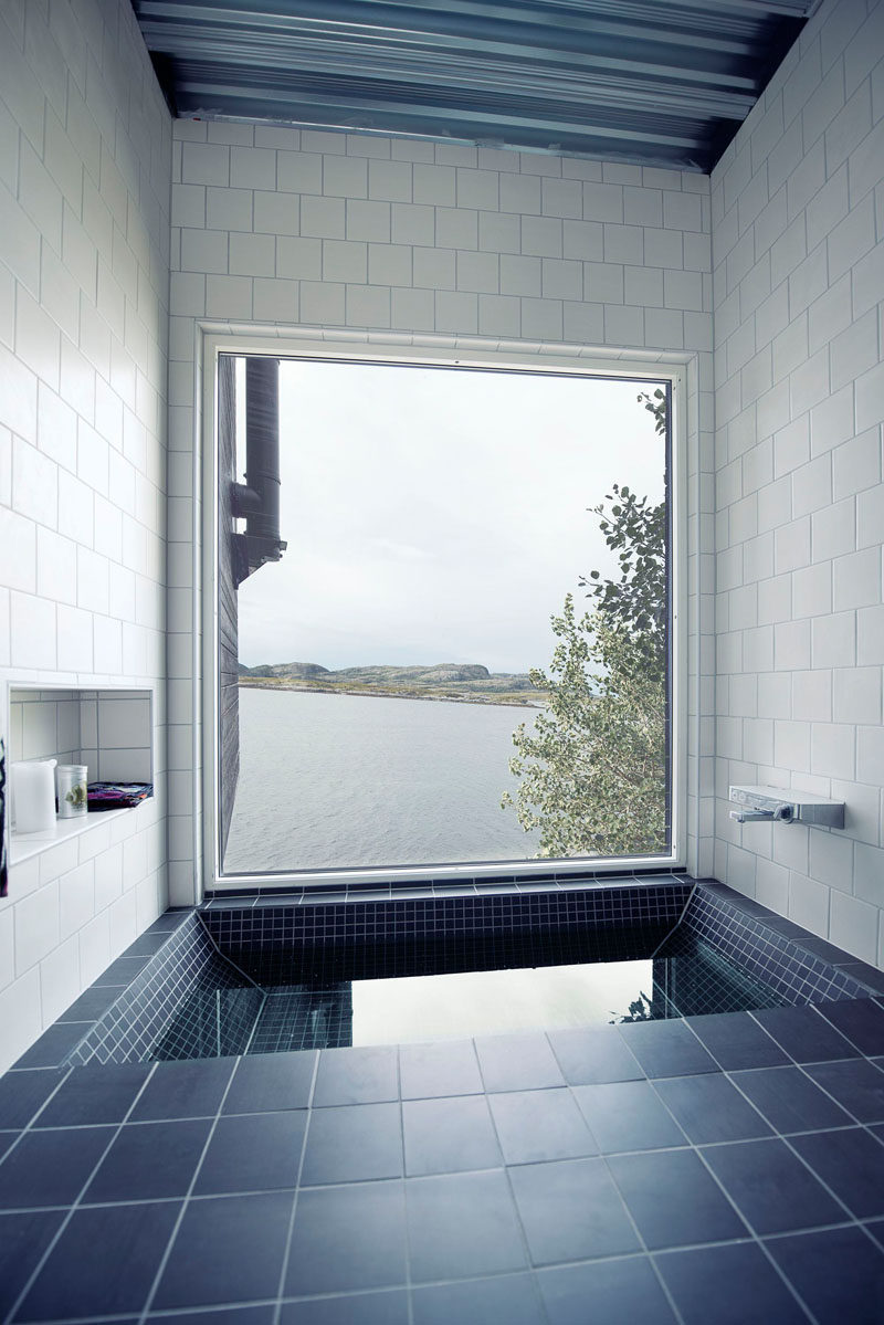 This bathroom in a small home in Norway has a built-in bathtub surrounded by gray and white tiles, and is perfectly positioned for water views.