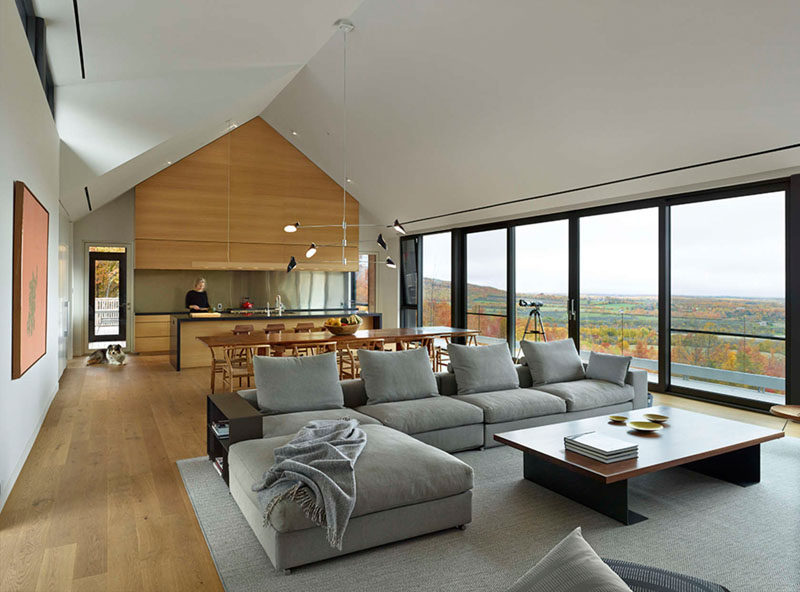 Inside this home, a wall of floor-to-ceiling windows match a door that opens to the balcony. The main floor with a peaked roof, is open plan with the kitchen, dining and living area all in the same room.