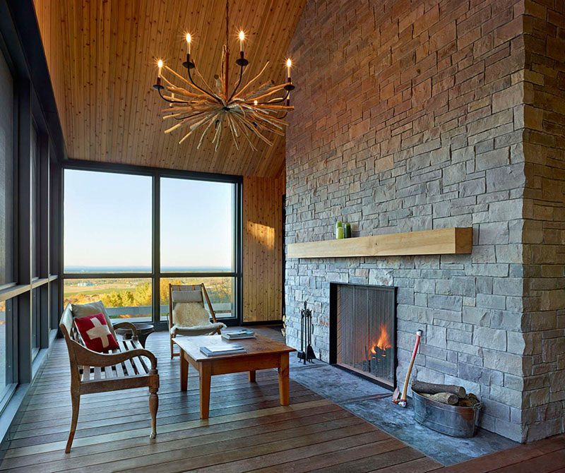 This casual sitting room focused on the fireplace is surrounded by windows and a wood floor and ceiling.