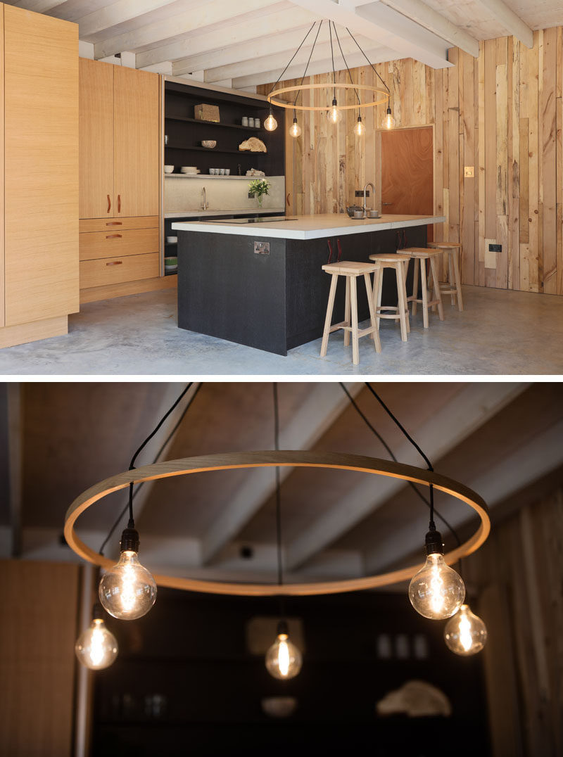 In this kitchen, the island is highlighted by a large hanging light, and the black in the island and cabinetry creates a dramatic contrast against the surrounding wood.