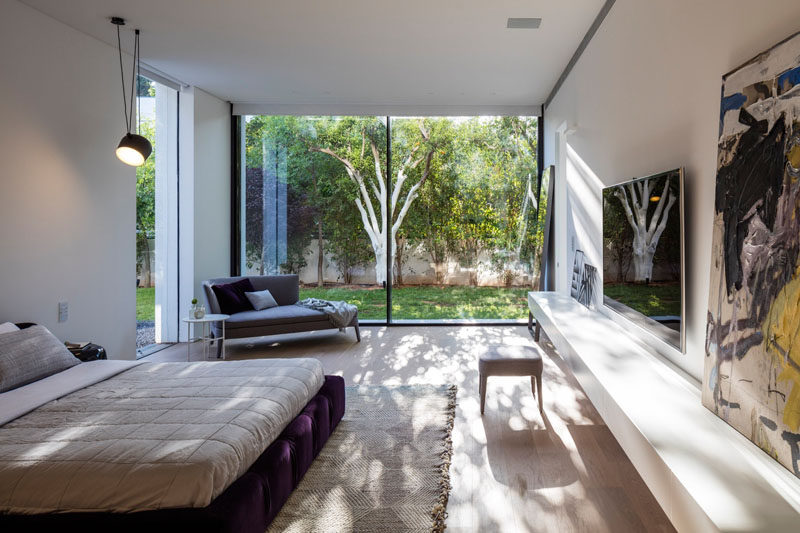 This bedroom has a view of the garden through floor-to-ceiling windows, and a low shelf for displaying artwork.