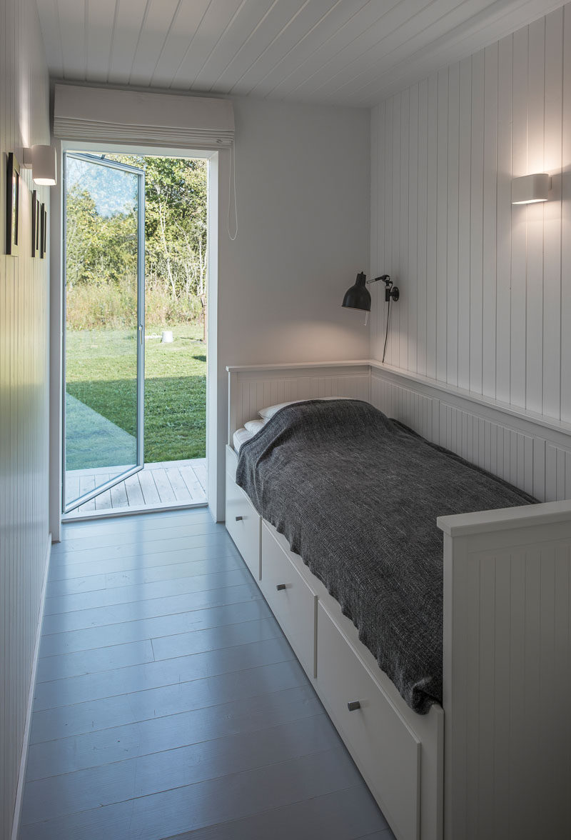 In this small bedroom, white wood paneling on the walls and ceiling make the room appear larger, and there's also has a door to the garden outside.