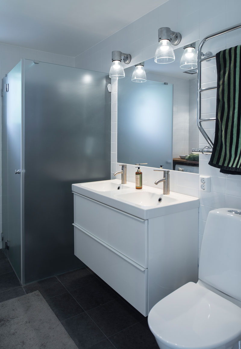 In this bathroom, white walls and cabinetry contrast with the dark floor, and there's a frosted glass shower enclosure.