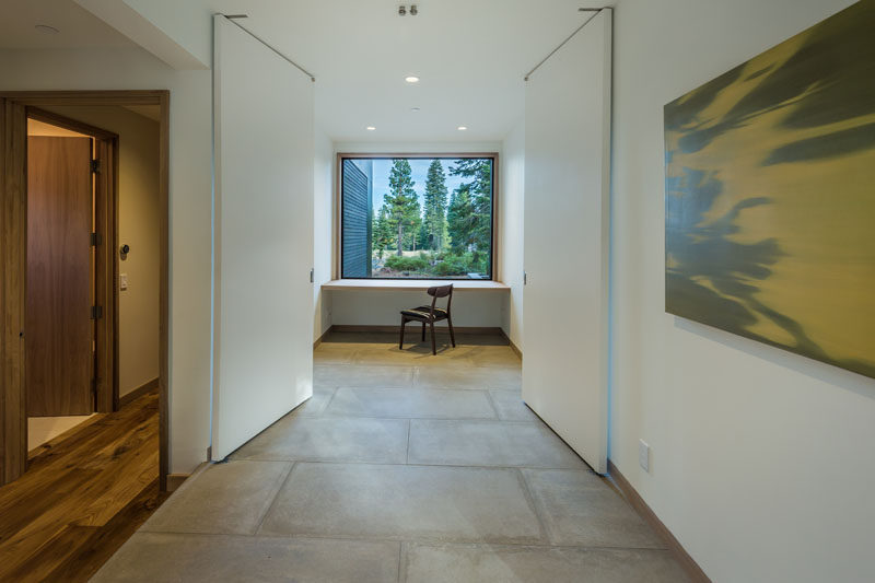 This home office with a built-in desk has a large picture window with views of the trees outside.