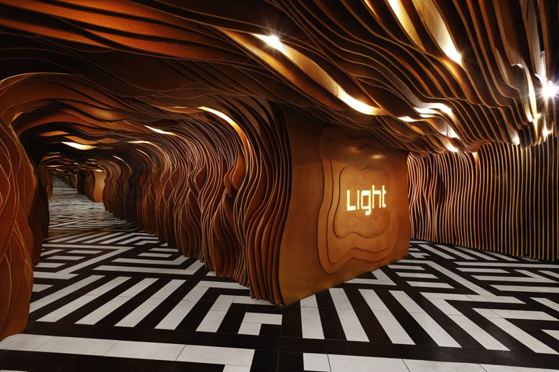 Inside the entrance of this nightclub, wooden panels with organic curves and hidden lighting guide you through to the main space, while a mirror on the wall makes the space seem endless.