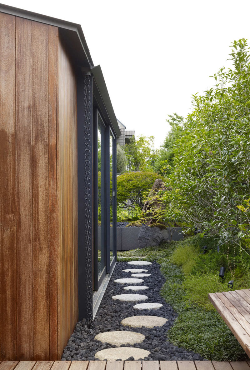 14 Modern Homes That Use Rain Chains To Divert Water // This rain chain, made from a traditional chain, is hidden next to the extended window frame on the side of this house and guides water in between the rocks of the footpath.