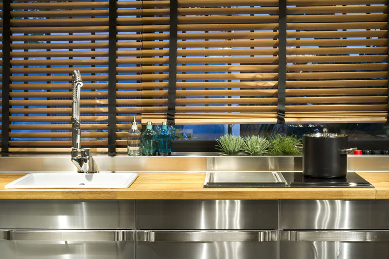 Wood Venetian blinds have been used to cover the windows in a steel kitchen.