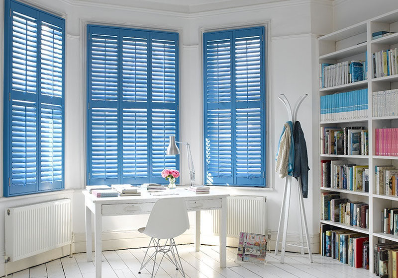 Blue louvres cover the bay windows and add color to the wall white home office.