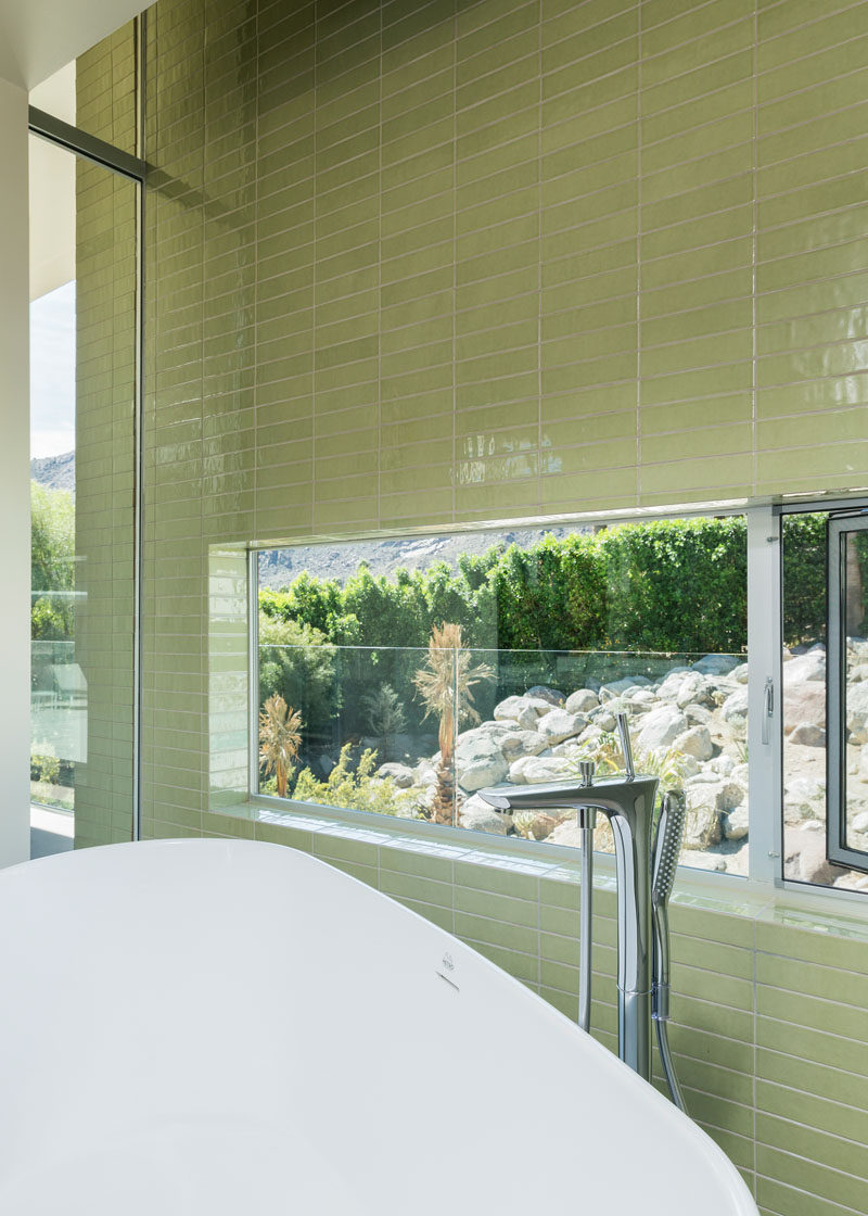 In this master bathroom, green tiles have been used to create a feature wall, and a window allows for picturesque views while having a relaxing bath.