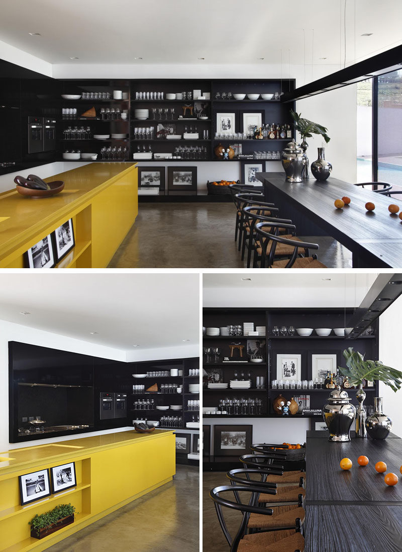 A yellow kitchen island adds a bright pop of color to the otherwise black cabinetry and shelving in the rest of the kitchen.