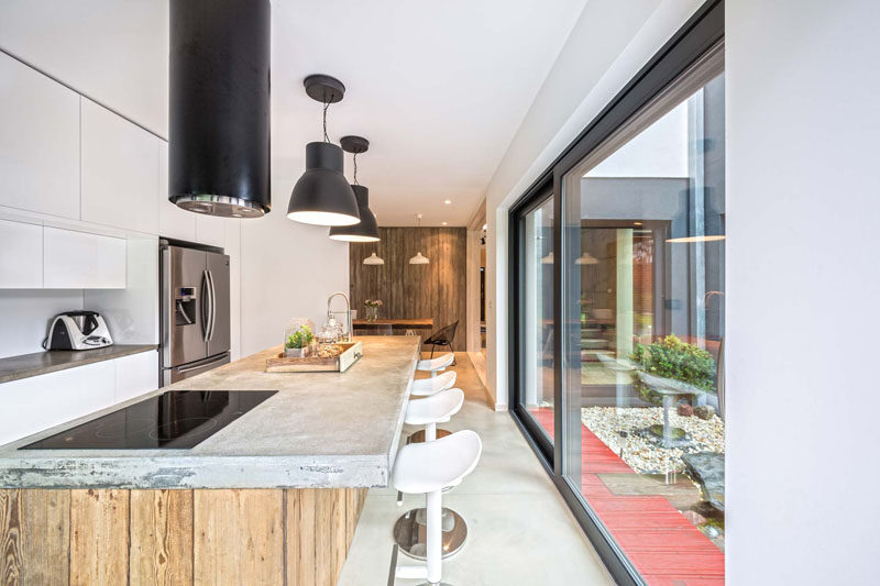 In this contemporary kitchen, a long concrete and wood island has ample room for seating and plenty of prep space. Large glass sliding doors give the kitchen access to the backyard.