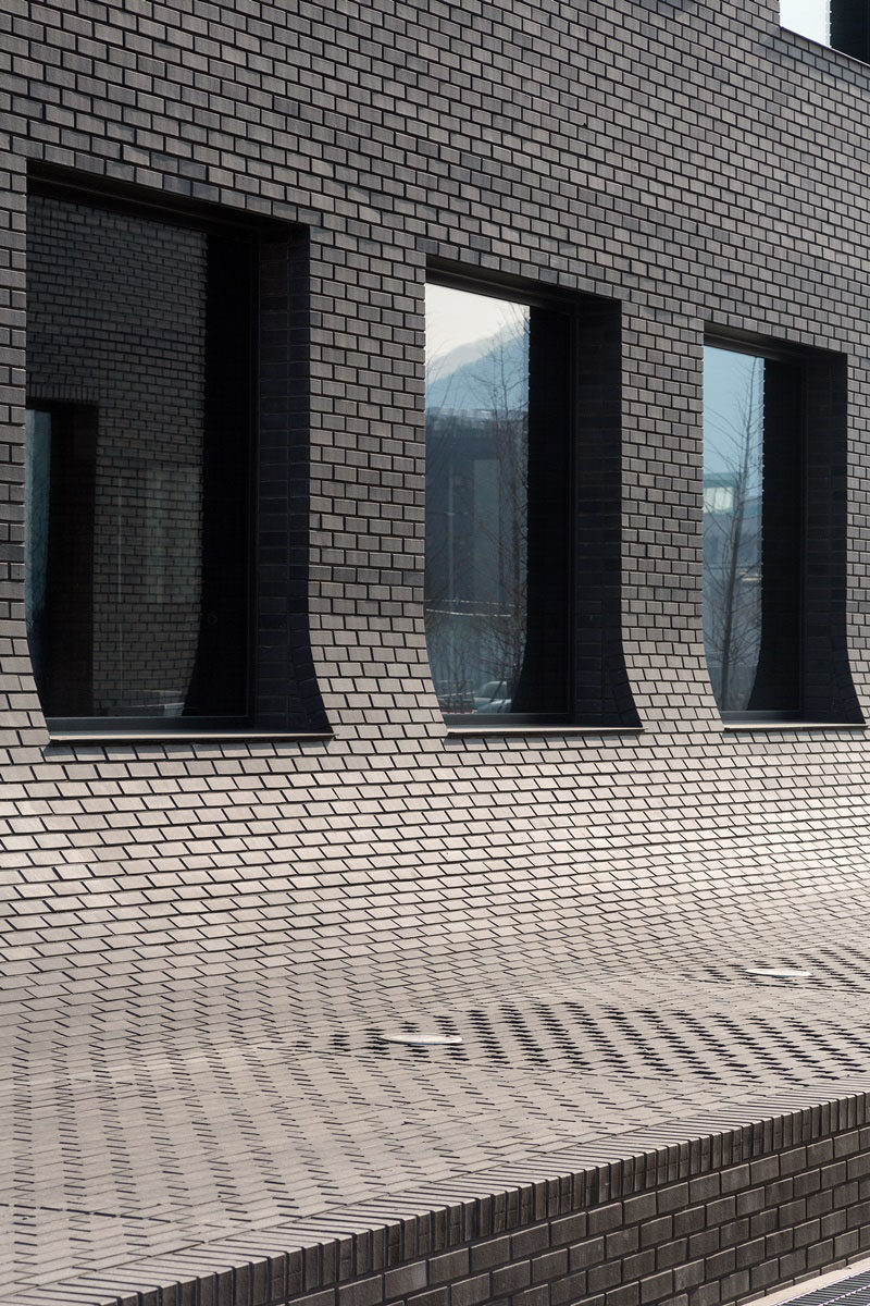 This black brick building in Korea curves down to meet the sidewalk.