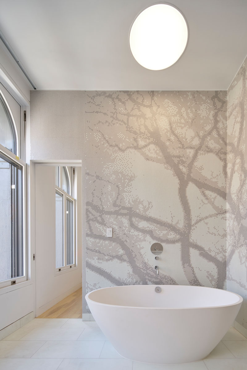 This renovated bathroom has a standalone tub surrounded by tile mural.