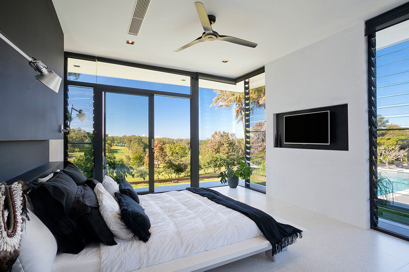 Floor-to-ceiling windows almost surround this modern black and white master bedroom and provide views of the backyard.