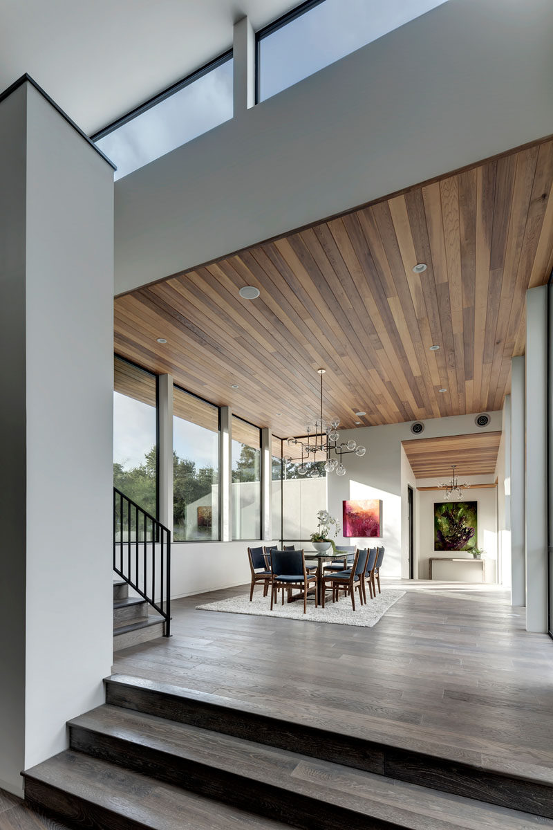 In this dining area, a high ceiling covered in wood, large windows, and large contemporary chandelier make the space feel dramatic.