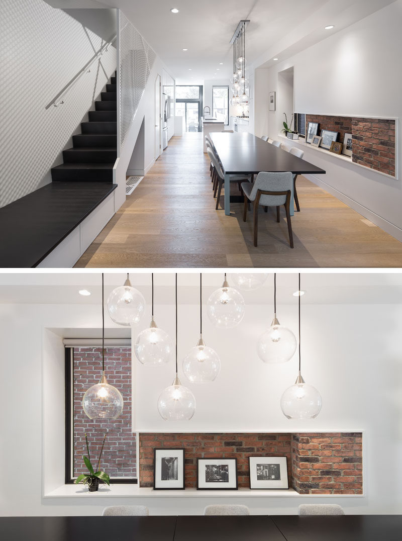 Inside this renovated home, the interior has been brightened up with bright white walls and a light colored wood floor. A glimpse of the original brick wall has been incorporated into a small shelving nook beside the dining table.